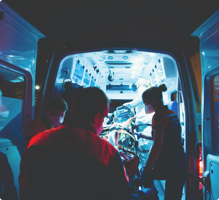 Picture of 2 people loading a patient in a stretcher on to a non emergency ambulance